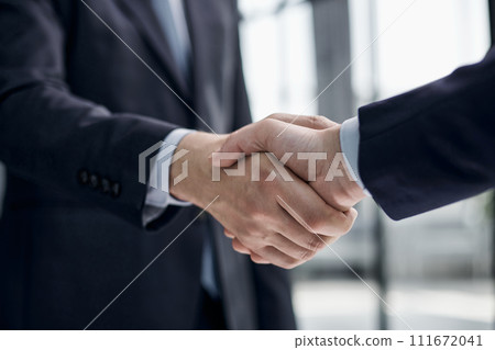 executives shaking hands in front of their manager and a colleague 111672041
