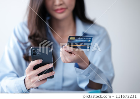 Close up Asian woman with smart phone and credit card, she fills in credit card information to pay for goods and services, online shopping concept pay by credit card via smartphone. 111672231
