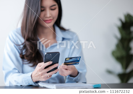 Close up Asian woman with smart phone and credit card, she fills in credit card information to pay for goods and services, online shopping concept pay by credit card via smartphone. 111672232