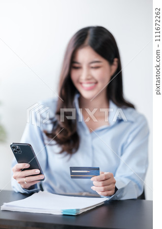 Beautiful Asian woman with smart phone and credit card, she fills in credit card information to pay for goods and services, online shopping concept pay by credit card via smartphone. 111672262
