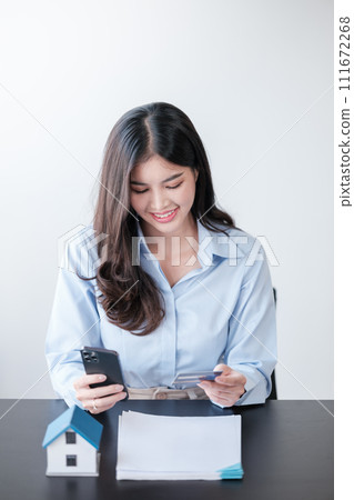 Beautiful Asian woman with smart phone and credit card, she fills in credit card information to pay for goods and services, online shopping concept pay by credit card via smartphone. 111672268