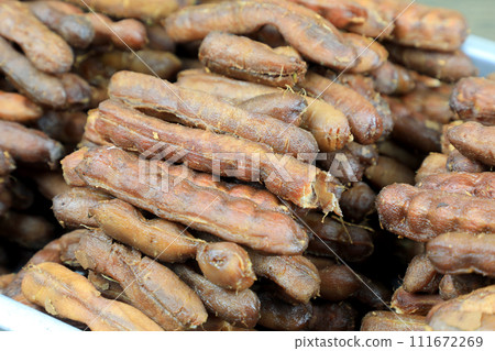 Tropical tamarind fruit without a shell, with visible seeds and inner pulp, in a galvanized tray on a wooden. Concept of food preservation in Thai style. Peeled tamarind is a ready-to-eat concept. 111672269