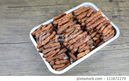 Tropical tamarind fruit without a shell, with visible seeds and inner pulp, in a galvanized tray on a wooden. Concept of food preservation in Thai style. Peeled tamarind is a ready-to-eat concept. 111672270