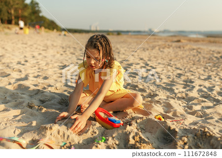 girl of 7 years old in yellow dress play with sand and toys on beach by sea girl of 7 years old in yellow dress play with sand and toys on beach by sea 111672848