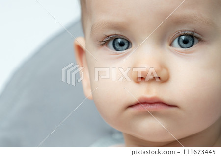 Close up of a babys face with blue eyes, looking at the camera 111673445