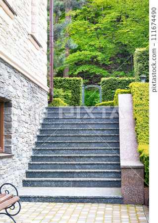 The steps of the granite staircase rise up along the wall of the beautiful estate and trimmed boxwood bushes. The steps of the granite staircase rise up along the wall of the beautiful estate and trimmed boxwood bushes. 111674490