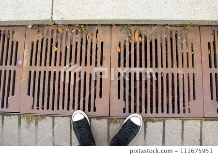 The sewer grate on the sidewalk is rusty 111675951