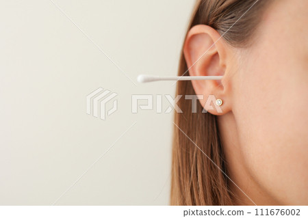 Cropped shot of unrecognisable young woman with cotton swab in ear isolated on white background. Close up female uses hygienic stick for cleaning ear. Daily habit routine. Hygiene and health care. Cropped shot of unrecognisable young woman with cotton swab in ear isolated on white background. Close up female uses hygienic stick for cleaning ear. Daily habit routine. Hygiene and health care. 111676002