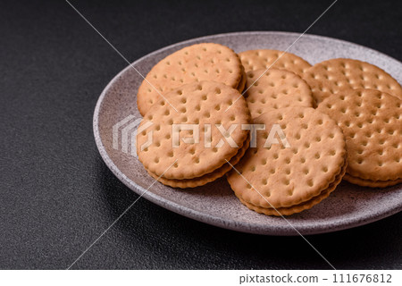 Round dotted snack snack cookies with cream on a dark concrete background Round dotted snack snack cookies with cream on a dark concrete background 111676812