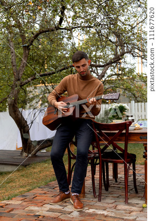 young man sits at the table and plays the guitar 111677620