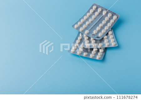 Medical background of many white capsule tablets or pills on blue table Medical background of many white capsule tablets or pills on blue table 111678274