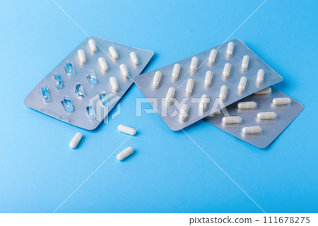 Medical background of many white capsule tablets or pills on blue table Medical background of many white capsule tablets or pills on blue table 111678275