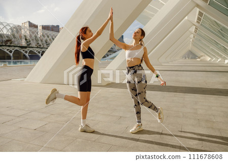 Happy female friends doing gesture of sport shake hand after exercising outside 111678608