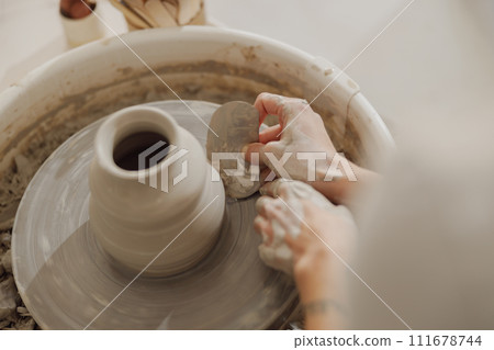 Close up of hands of professional potter molding pot shape on pottery wheel. Ceramics art concept Close up of hands of professional potter molding pot shape on pottery wheel. Ceramics art concept 111678744