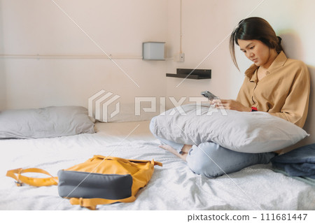 Asian woman sit on the bed in a small bedroom of budget hotel. Asian woman sit on the bed in a small bedroom of budget hotel. 111681447