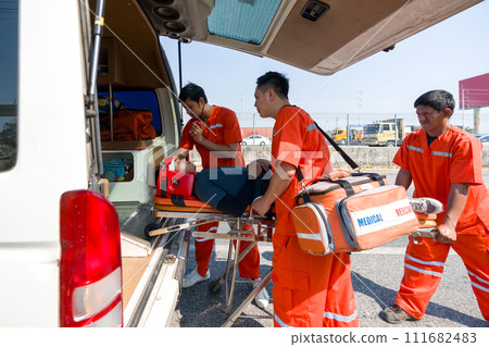 Group of male nurse in an orange uniform places a neck and head accident victim on a bed in an ambulance. 111682483