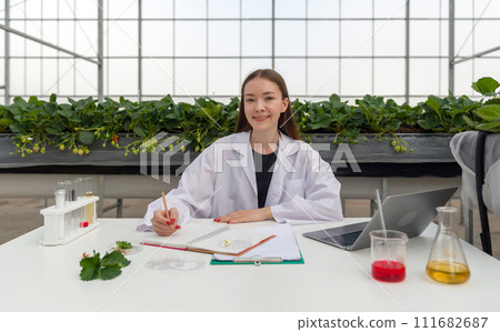 A scientist conducting research with a laptop within a vegetation-rich greenhouse. 111682687