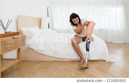 Asian woman disability with prosthetics bionic leg, prosthetic limbs sitting in bedroom at home. Asian woman disability with prosthetics bionic leg, prosthetic limbs sitting in bedroom at home. 111682692