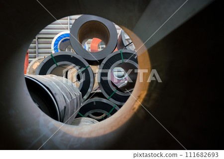 Stacks of silver steel coils sit piled in a large, busy factory setting. Stacks of silver steel coils sit piled in a large, busy factory setting. 111682693