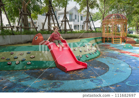 A child is going down a slide with a happy face at a playground full of colorful equipment. 111682697