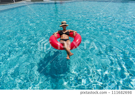 A lady enjoy a sunny day, floating on a bright inflatable ring in a clear blue swimming pool. A lady enjoy a sunny day, floating on a bright inflatable ring in a clear blue swimming pool. 111682698