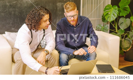 Two coworkers talking while using laptop sitting 111686045