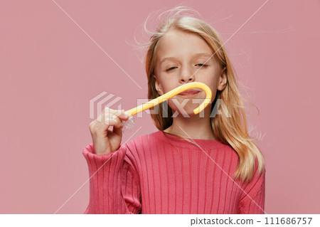 Happy Schoolgirl with Pink Lollypop A stylish and adorable young girl with a joyful smile poses in a studio setting Surrounded by a vibrant pink background, her expressive face reflects the fun and Happy Schoolgirl with Pink Lollypop A stylish and adorable young girl with a joyful smile poses in a studio setting Surrounded by a vibrant pink background, her expressive face reflects the fun and 111686757