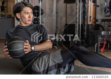 Asian man doing abdominal muscle training using a medicine ball at the gym (Russian twist/twist crunch) 111688320