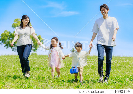 A family walking hand in hand through a meadow under the blue sky A family walking hand in hand through a meadow under the blue sky 111690309