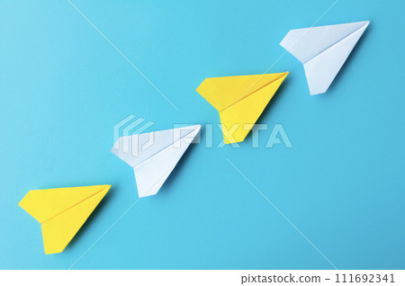 Top view of white and yellow paper airplanes origami flying on blue background 111692341