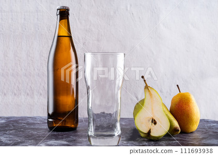 Empty glass near bottle and pear. A slice of pear and a glass. 111693938