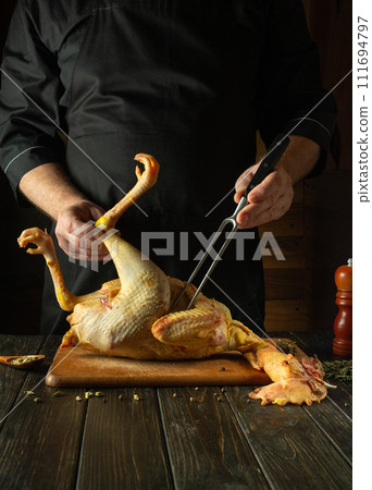 A dish of raw chicken by the hands of a chef in a restaurant kitchen. Concept of cooking raw rooster on a cutting board. Fork in the hand of the cook A dish of raw chicken by the hands of a chef in a restaurant kitchen. Concept of cooking raw rooster on a cutting board. Fork in the hand of the cook 111694797