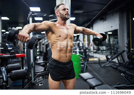 Determined Caucasian male bodybuilder working out chest muscles, using heavy dumbbells. Side view of crossfit man exercising in modern gym at evening. Concept of sport, bodybuilding, health. Determined Caucasian male bodybuilder working out chest muscles, using heavy dumbbells. Side view of crossfit man exercising in modern gym at evening. Concept of sport, bodybuilding, health. 111696049