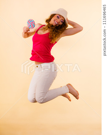Positive woman jumping holds lollipop candy in hand 111696465