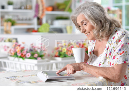Beautiful senior woman using tablet at home 111696543