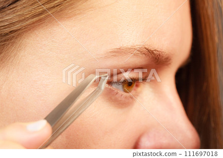 Woman tweezing eyebrows depilating with tweezers 111697018