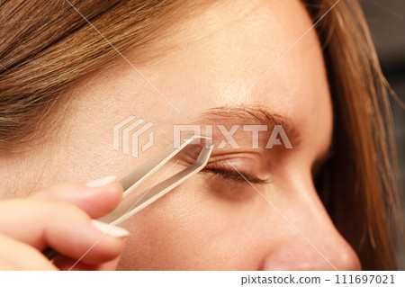 Woman tweezing eyebrows depilating with tweezers Woman tweezing eyebrows depilating with tweezers 111697021