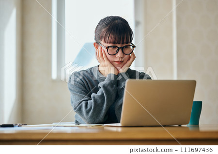 一位年輕女子背著下巴看著電腦思考 一位年輕女子背著下巴看著電腦思考 111697436