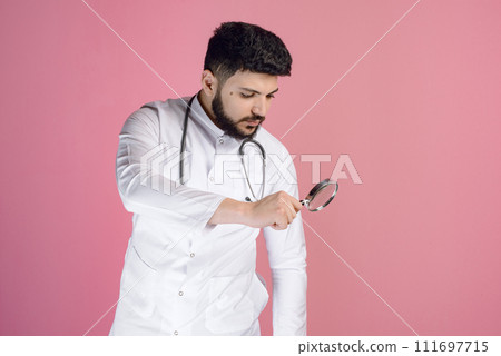 Side view of brunette male doctor, intern, paramedic in uniform standing, holding magnifying glass. Concept of medicine. 111697715