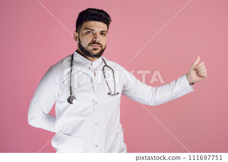 Front view of handsome male doctor, intern wearing uniform with phonendoscope, looking at camera. Isolated on pink studio background. Front view of handsome male doctor, intern wearing uniform with phonendoscope, looking at camera. Isolated on pink studio background. 111697751
