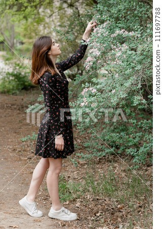 Side view of attractive girl standing in blooming garden, touching blossom, looking up, admiring. Concept of springtime. 111697788