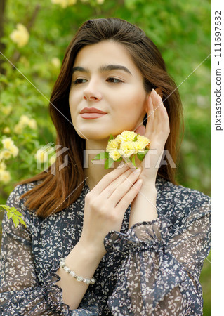 Side view of pretty, brunette girl standing in blooming park, holding blossom, flower, looking forward. Concept of springtime. 111697832