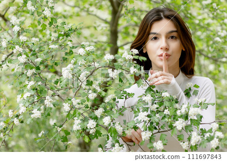 Front view of attratctive, young female having photoshoot in park, garden, looking at camera, showing quiet. Concept of springtime. 111697843
