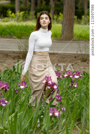 Side view of attractive, slim, brunette female walking in flowers in garden, looking aside, enjoying. Concept of springtime. 111697986