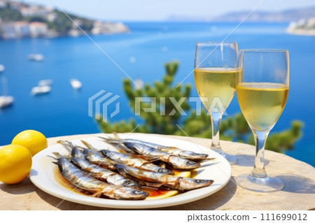 Grilled Sardines served in the restaurant at outdoor terrace with lemons and glasses of white wine 111699012