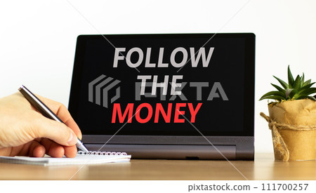 Follow the money symbol. Concept words Follow the money on beautiful tablet screen. Beautiful wooden table white background. Businessman hand. Business and follow the money concept. Copy space. 111700257
