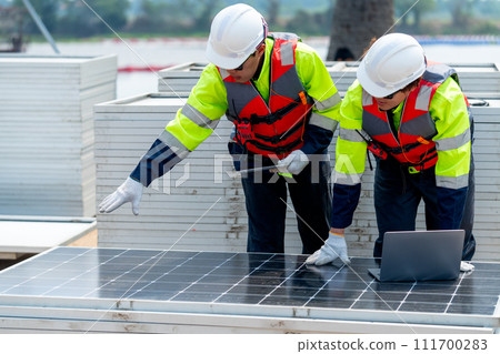 Two Asian professional technician workers stand near solar cell panel and use laptop to discuss about work in concept of green energy system for good environment. Two Asian professional technician workers stand near solar cell panel and use laptop to discuss about work in concept of green energy system for good environment. 111700283