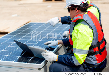 Side view and close up two Asian professional technician workers sit near solar cell panel and use laptop to discuss about work in concept of green energy system for good environment. 111700285