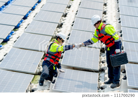 Two professional technician workers with safety uniform check hands for the success of work during work with solar cell panels system over water reservoir. 111700290
