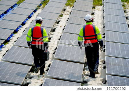 Back of professional with safety uniform walk on footpath along row of solar cell panels in workplace concept of green energy power plant for good environment. Back of professional with safety uniform walk on footpath along row of solar cell panels in workplace concept of green energy power plant for good environment. 111700292